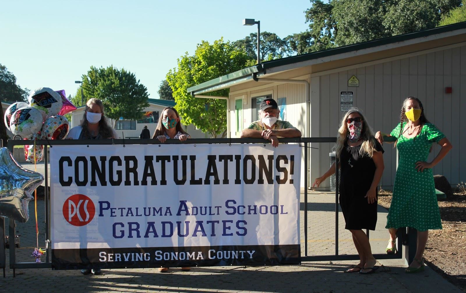 Petaluma Adult School graduation 2020 banner with five masked staff standing around it