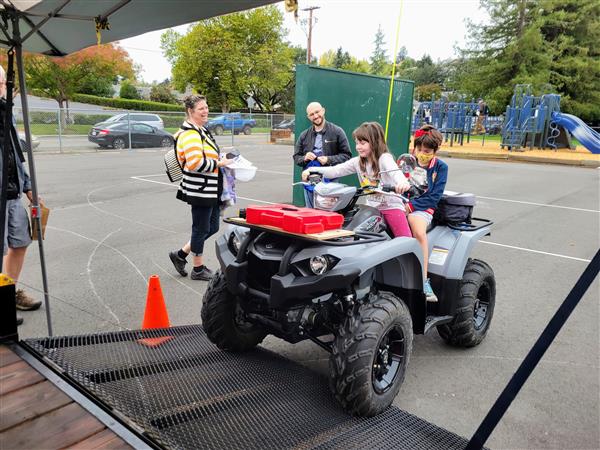 Two kids smiling on an ATV at a school event.