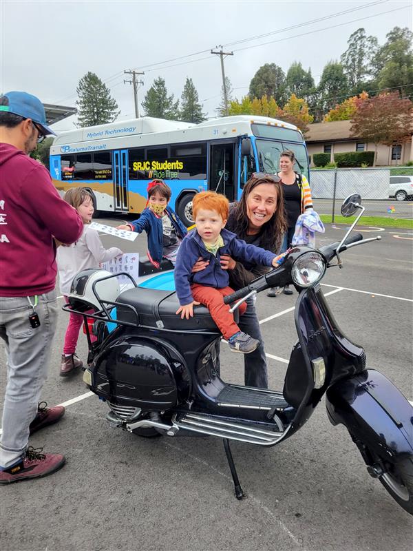 Red headed preschooler sitting on a vespa at a school event.