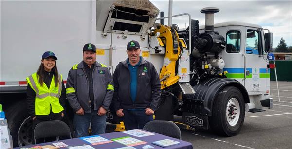 Recology workers smiling in front of their truck at a school event.