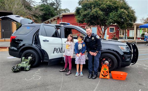 Two kids in front of a police car with a police officer at a school event.