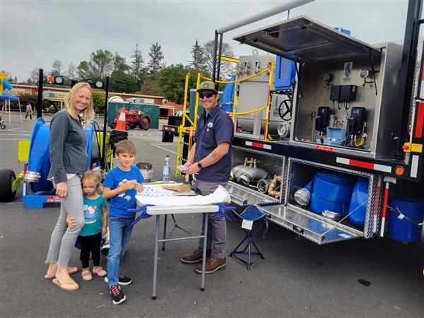 Woman and two children talk to a man about a Water Maintenance Truck.  