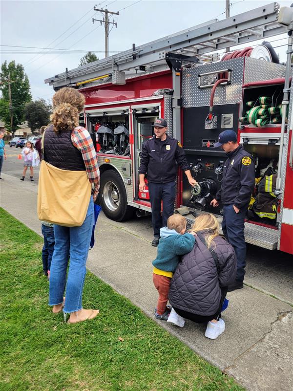 A small crowd listens to two firefighters.